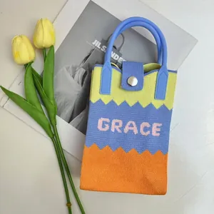 Detail of knitted phone bag with wave patterns and Grace embroidery on a white surface
