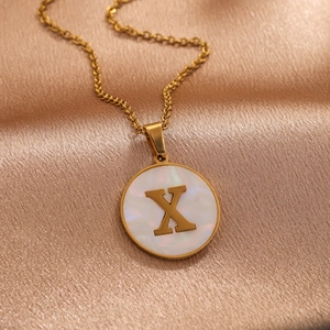 Golden stainless steel letter X necklace with white shell pendant on silk background