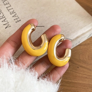 Détail de boucles d'oreilles C en émail jaune et or tenues dans un cadre de style de vie