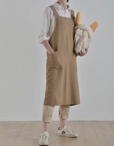 Detail of light brown linen apron featuring dual front pockets and durable cross-back straps