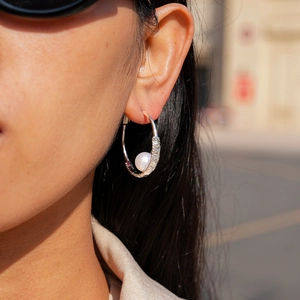 Detail of silver hoop earrings with woven texture and a single pearl accent on model