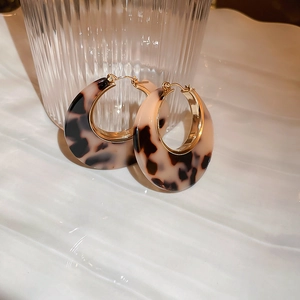 Detail of round leopard print resin hoop earrings with gold metal clasp on white ceramic