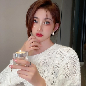 French luxury pearl earrings and silver rings worn with a white cable knit sweater