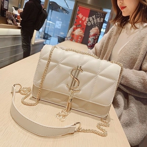 Close-up of white quilted leather crossbody bag with gold logo pendant and tassel detail