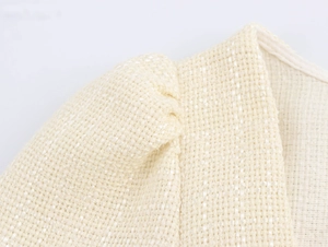 Détail de la robe en tweed beige élégante montrant la texture et la couture bouffante