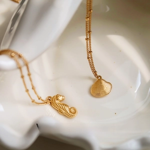 Macro detail of gold seahorse and shell pendants on beaded chain in a ceramic tray