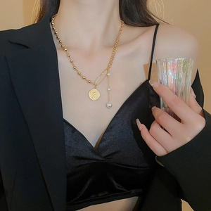 Close-up of gold coin portrait necklace with safety pin and pearls on neck