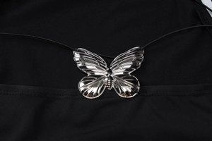 Detailed macro view of the silver butterfly metal pendant on the black fabric backless dress