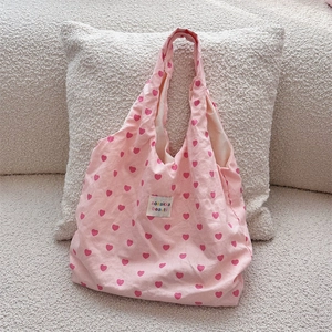 Close-up of pink canvas tote bag featuring red heart patterns and woven label detail