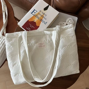 Detail of white quilted tote bag featuring shell pattern stitching and French label