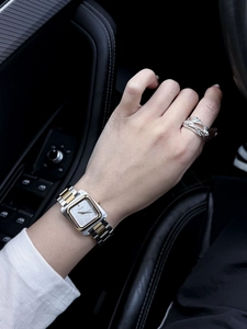 Gros plan d'une montre carrée bicolore et d'une bague argentée portée au poignet