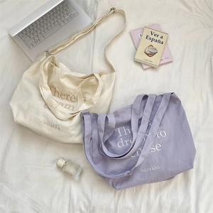 Close-up of canvas tote bags in cream and lilac with letter embroidery on white fabric