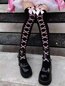 Detail of black thigh-high stockings with pink bows and crossbone prints on stone steps