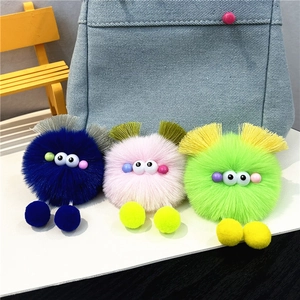 Detail of colorful plush monster keychains in pink, blue, and green on a denim bag