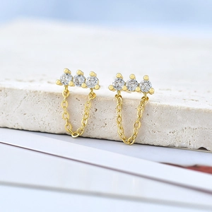 Macro shot of gold S925 earrings featuring three sparkling zircons and delicate chain drops