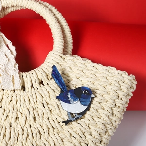 Blue acrylic magpie bird brooch pinned on a beige woven straw bag as fashion accessory