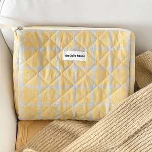 Detail of yellow checkered quilted makeup bag with zipper and logo label on white leather