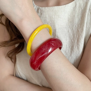 Detail view of resin bangle set featuring yellow slim ring and red marble pattern texture