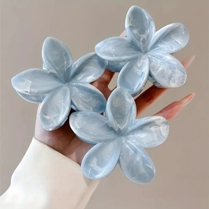 Close-up of three light blue acetate flower hair claws with marble texture held by hand