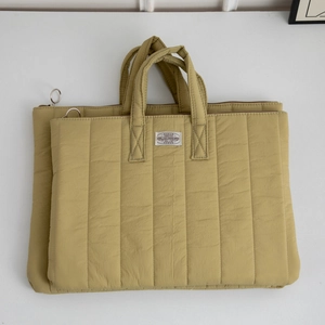 Close-up of mustard yellow quilted laptop bag set with vertical stitching and metal zippers