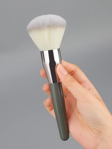 Close-up of a large powder brush with soft gradient bristles and dark green handle