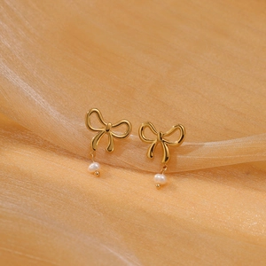Close-up of elegant gold bow earrings with a white pearl pendant on silk fabric