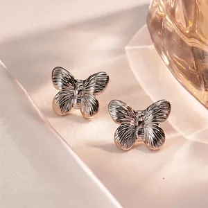 Macro detail of silver butterfly earrings with fine texture on soft silk background