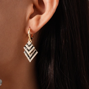 Macro shot of gold hoop earrings with black and white diamond-set geometric rhombuses