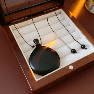 Close-up of a smooth faux wood gourd pendant on a brown woven rope in a luxury gift box
