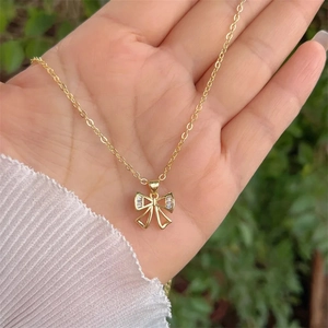 18K gold plated necklace featuring a sparkling cubic zirconia bow pendant held by hand