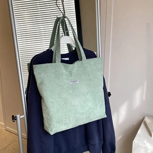 Close-up of green corduroy tote bag featuring vertical texture and a fashion label