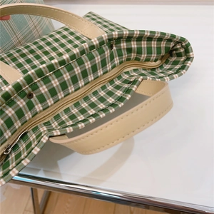 Detail view of the green checkered tote bag with leather handles and zip closure
