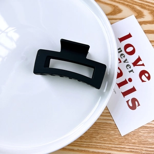 Macro view of a matte black rectangular hair claw clip on a white ceramic plate