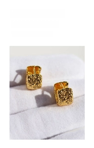 Macro detail of gold earrings featuring irregular lava texture and crinkle foil finish