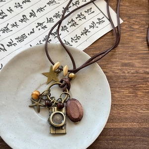 Close-up of vintage bronze camera and star pendants on wax rope necklace with wooden beads