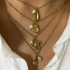 Layered gold necklace featuring sea shell, turtle, and seahorse pendants with pearls