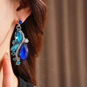 Close-up of vintage rhinstone diamond-shaped earrings with blue crystals on model