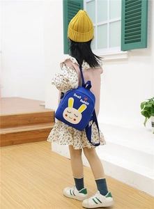 Toddler girl wearing blue cartoon rabbit canvas backpack shown from a side back view