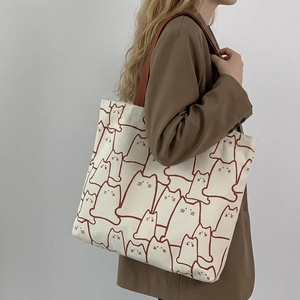 Minimalist canvas tote bag with cat print and brown handles shown on female shoulder