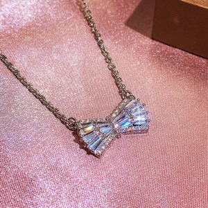 Detail of silver bow pendant necklace with cubic zirconia on pink glitter fabric