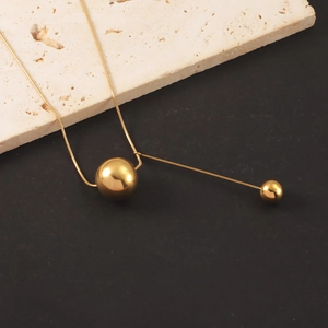 Detail of a gold stainless steel ball pendant necklace on a beige stone texture
