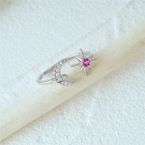 Macro view of silver star and moon ring with magenta gemstone on a wooden branch