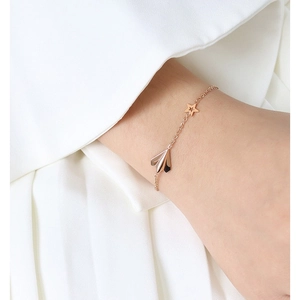 Rose gold chain bracelet with paper airplane and star charms on model wrist