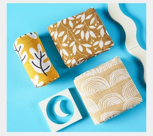Three pieces of soft muslin baby swaddle blankets in yellow and brown organic patterns