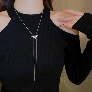 Macro shot of gold triangular rhinestone pendant with long tassel chain on black sweater