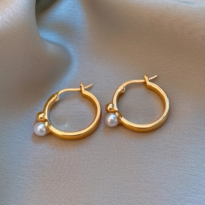 Détail de créoles plaquées or 14K avec perles blanches sur fond de soie grise brillante