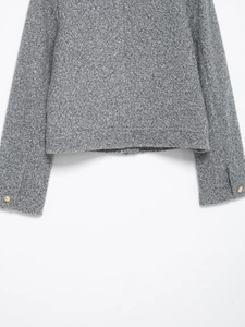 Detailed close-up of grey tweed jacket fabric with embossed gold metal buttons and hem