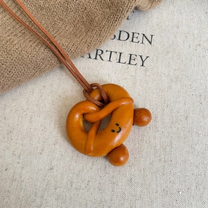 Cute croissant pretzel smile face pendant necklace with brown leather cord on fabric