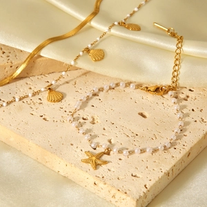 Dettaglio set bracciali dorati con stelle marine su travertino beige e tessuto di seta