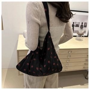 Close-up of black corduroy shoulder bag featuring red strawberry print worn by model